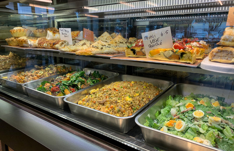 Display of various food items in a buffet setting with trays and signs.